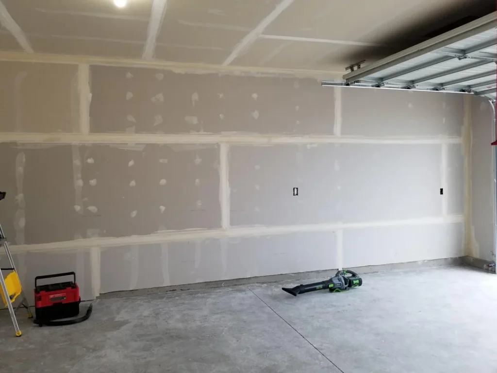 Wide garage wall with drywall seams and fastener spots prepared for finishing